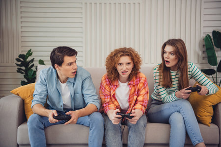 Funny young people enjoying video games together in a cozy living room setting with intense and...