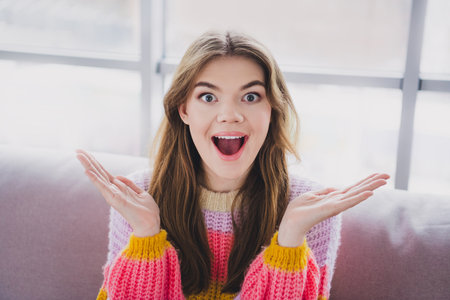 Excited young woman in colorful sweater expressing joy at home in a bright indoor setting