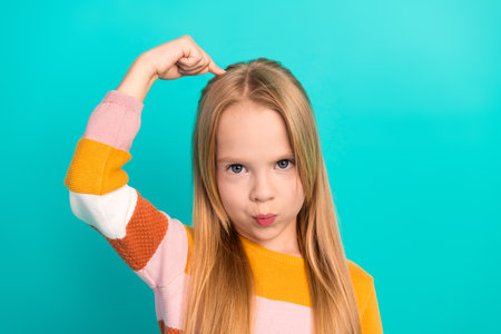 Confident young girl making a gesture expressing strength against a vibrant teal background,...
