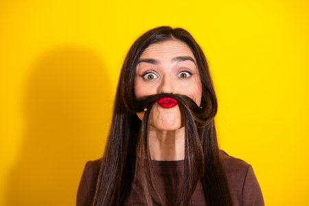 Playful portrait of a happy young woman mimicking a mustache against vibrant yellow background
