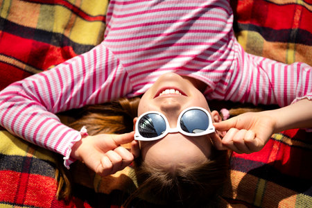 Smiling young girl with sunglasses enjoying a sunny day outdoors on a colorful blanket