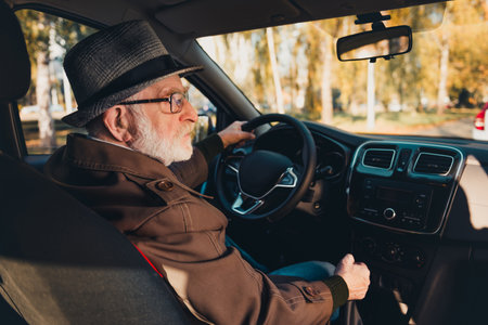 Elderly man driving through sunny autumn city streets enjoying the seasons natural beauty in his...