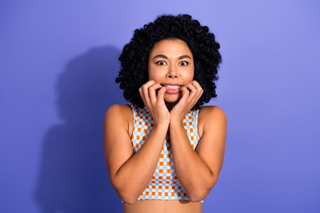 Excited young woman with curly hair expressing emotions against a purple background in trendy casual...