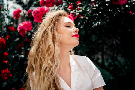 Young blonde woman enjoying outdoor sunlight with floral background in summer day