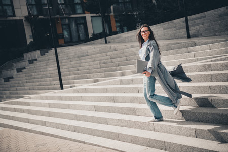 Elegant professional woman walking down urban stairs while holding a laptop and exuding confidence...