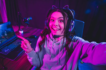 Young woman live streaming gameplay on laptop in neon lighting setup, casual gaming and content...