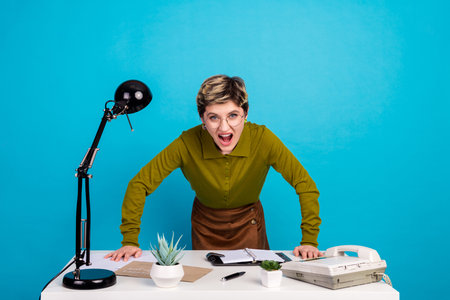 Young professional woman in green shirt leaning over work desk with a retro feel on blue backgroundの写真素材