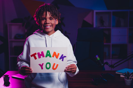 Young video blogger holding a thank you sign in a home media studio with neon lighting showcasing...