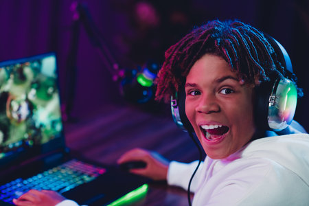 Young male gamer streaming online in a vibrant neon-lit room with a laptop, enjoying a gaming...