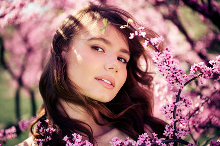 Charming young woman surrounded by blooming spring blossoms, exuding beauty and serenity in a sunny...