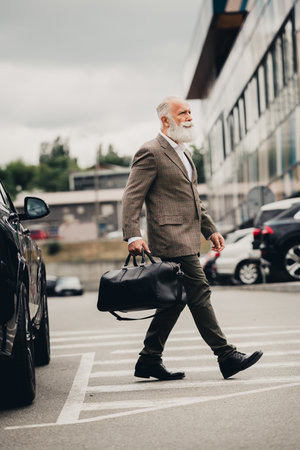 Handsome senior businessman walking outdoors carrying a bag near modern buildings demonstrating...