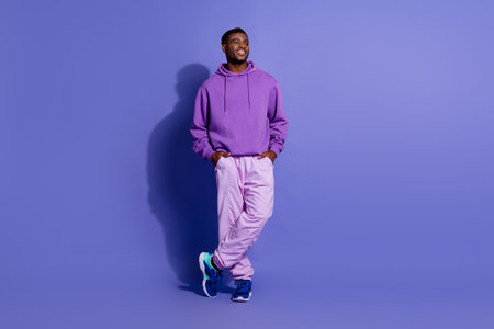 Young man in purple hoodie posing with a positive expression against a violet background, showcasing...