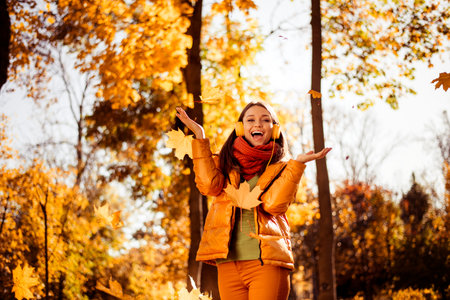 Young woman enjoying an autumn day outdoors surrounded by golden leaves in a park, radiating joy and...