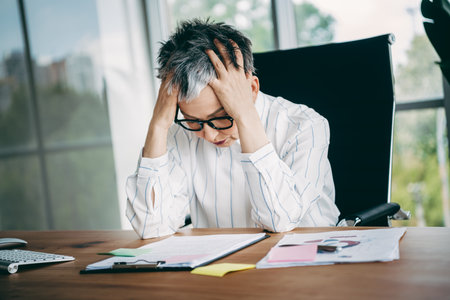 Stressed businesswoman in formal attire dealing with work challenges at her office desk in a...