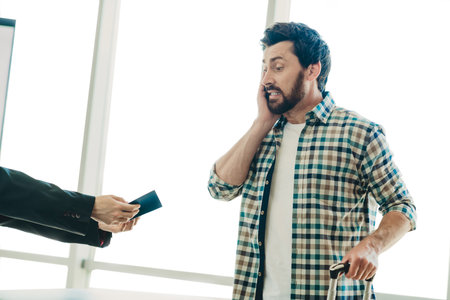 Casually dressed man in a vibrant terminal reacting while speaking on phone and handling luggage and...