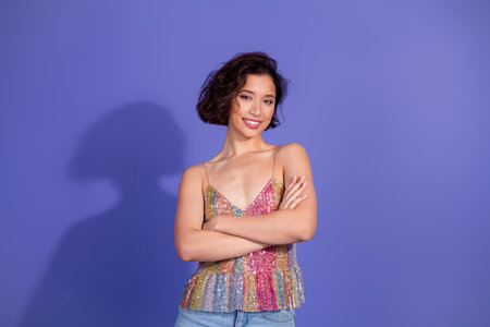 Charming young woman in casual glam outfit posing confidently on fashionable purple backdrop