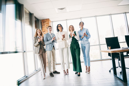 Young professionals in a stylish office celebrating success with smiles, applauding teamwork and...