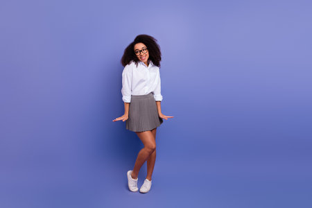 Young stylish woman in a white shirt and grey skirt standing against a vibrant violet background, full-length shotの写真素材