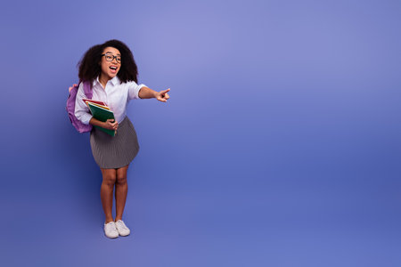 Happy young student with book pointing energetically over a violet background demonstrating enthusiasm and positivityの写真素材