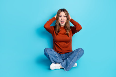 Cheerful young woman in casual outfit sitting against a blue background demonstrating vibrant and energetic expressionの写真素材