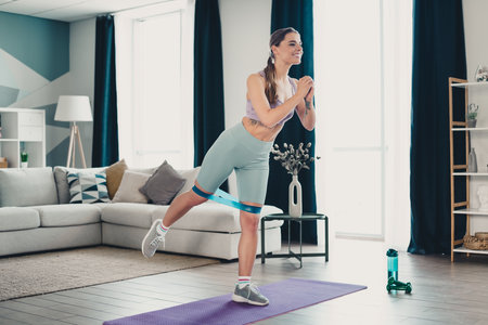 Sporty Young sportswoman exercising indoors with fitness band standing on matの写真素材