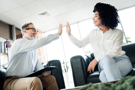 Business professionals exchange a high five in a modern office space, symbolizing teamwork,...