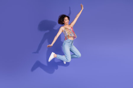 Young woman in colorful sequined top leaping joyfully against a vibrant purple background showcasing...
