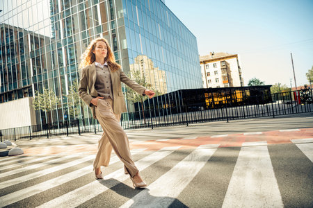 Confident businesswoman walking across an urban crosswalk on a sunny day with modern office buildings in the backgroundの写真素材