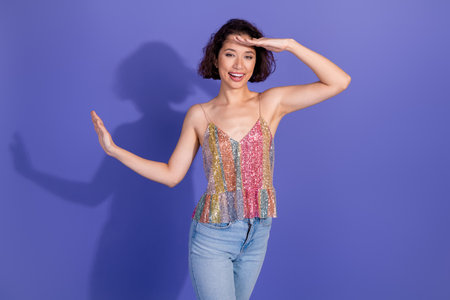 Fashionable young woman in a glittery top posing with a cheerful expression on a vibrant purple...