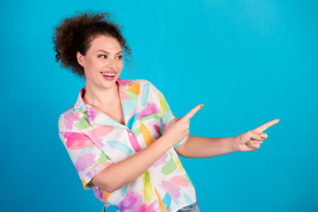 Smiling woman in colorful shirt making friendly gestures against a blue background