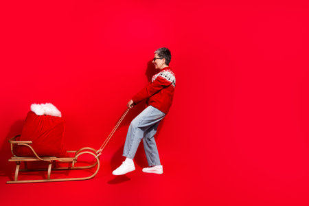 Joyful woman pulling a festive sled with a red sack against a vibrant red background celebrating the...
