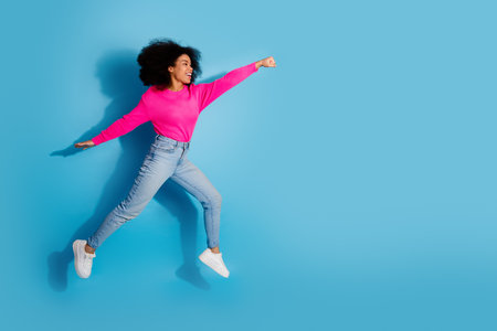 Young woman in vibrant casual outfit jumping on blue background symbolizing excitement, energy, and...