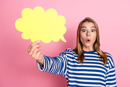 Surprised woman holding a yellow speech bubble against a pink background to convey communication...