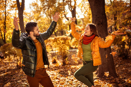Joyful couple enjoying an autumn day outdoors with golden leaves and warm sunlight in a scenic park...