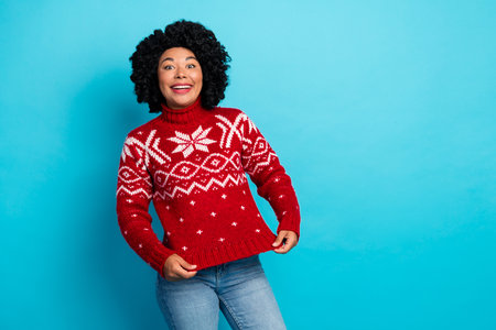 Cheerful young woman in festive red sweater on blue background celebrating the holiday season with a big smileの写真素材