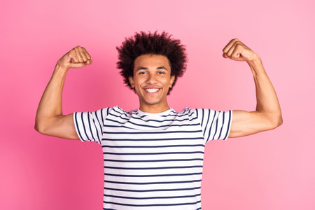 Energetic young man flexing his arms and smiling confidently against a vibrant pink background