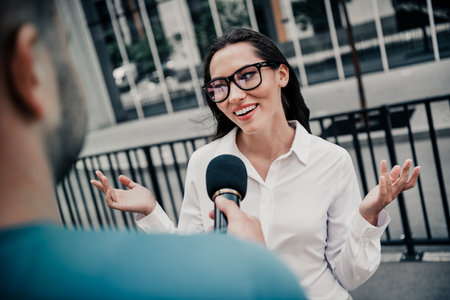 Businesswoman being interviewed outdoors on a city street, smiling and gesturing confidently in...