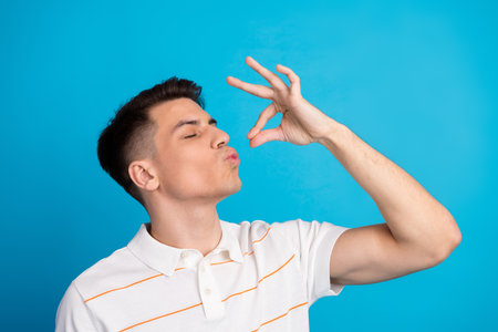 Young man gesturing with hand expressing appreciation in casual attire against a solid blue backdrop
