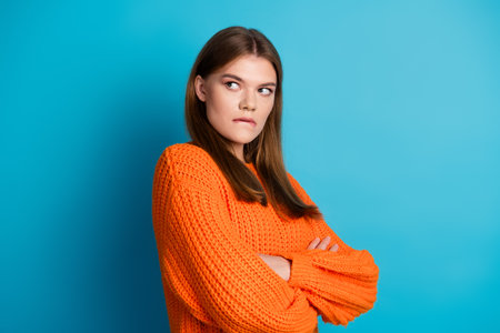 Young woman wearing a vibrant orange sweater posing against a vibrant blue backdrop with a...