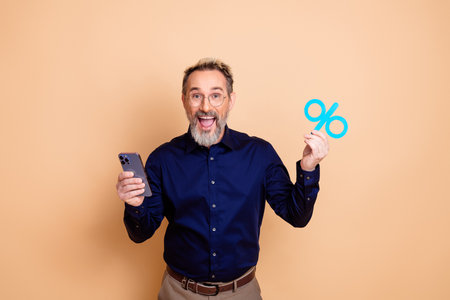 Excited man holding smartphone and percentage symbol on beige background showcasing discount or...