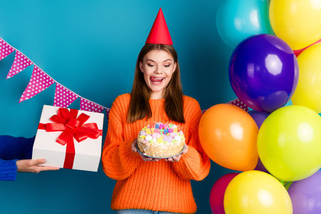 Cheerful young woman celebrating birthday with cake, balloons, and presents on a colorful festive...