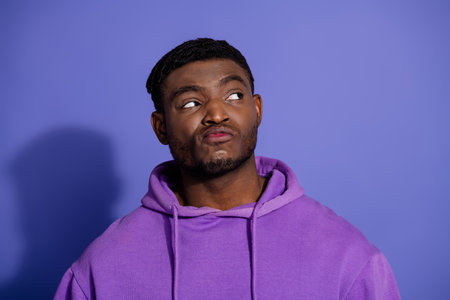 Young man in a casual purple hoodie standing against a bold violet background with a thoughtful...