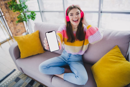Delighted young woman enjoying music at home while showing her smartphone screen in a comfortable...