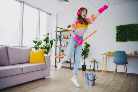 Charming woman enjoying a lively cleaning session at home, holding a mop in a stylish and modern...