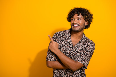 Smiling young man pointing with joy against a yellow background showcasing trendy style with a leopard print shirtの写真素材