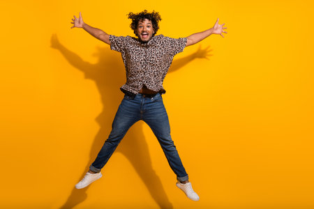 Young man jumping joyfully in a casual leopard print shirt against a bold yellow background,...