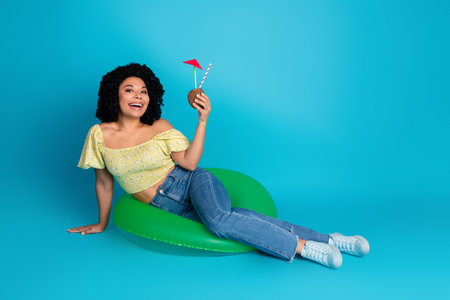 Charming young woman relaxing with a drink against a blue background, wearing fashionable casual...