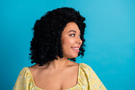 Portrait of a cheerful young woman with curly hair wearing a floral yellow top posing against a...