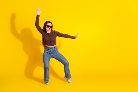Charming young woman strikes a funny dance pose in trendy outfit with yellow background, expressing...