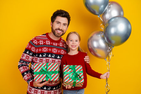 Dad and daughter celebrating Christmas together, holding gifts and balloons against a festive yellow...